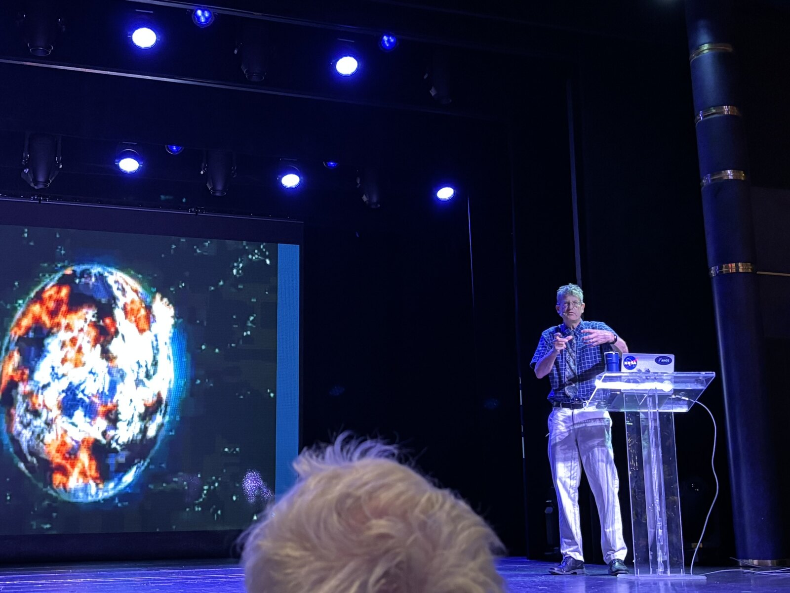 Meers Oppenheim giving a public lecture on stage, with a NASA image of the Sun projected behind him.