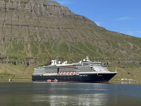 The cruise ship at anchor beneath steep fjord cliffs.