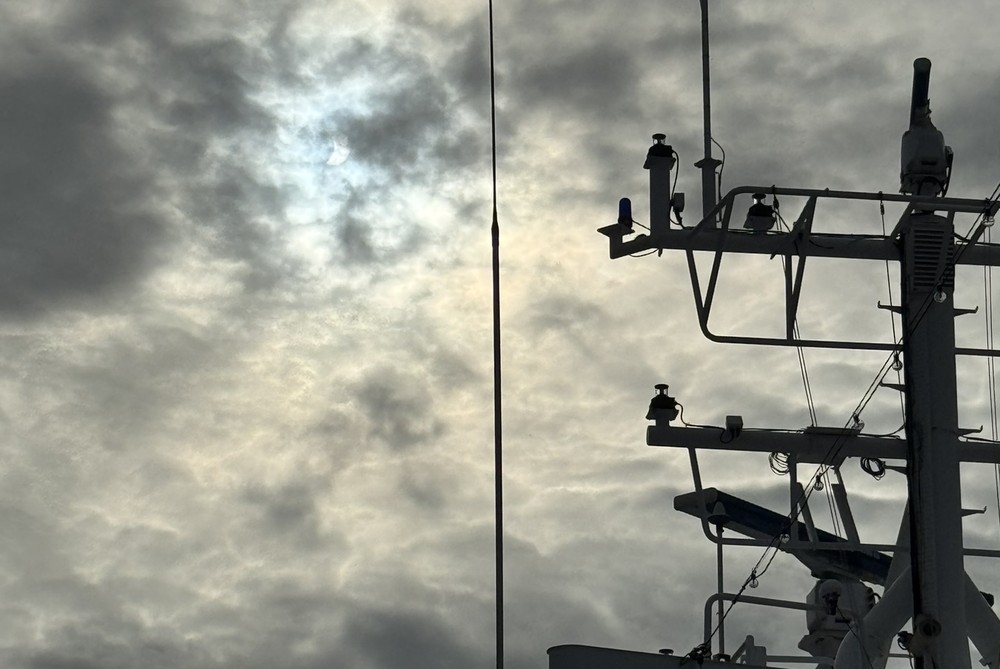 The partially eclipsed Sun glimpsed through clouds above the ship's mast, August 2026.