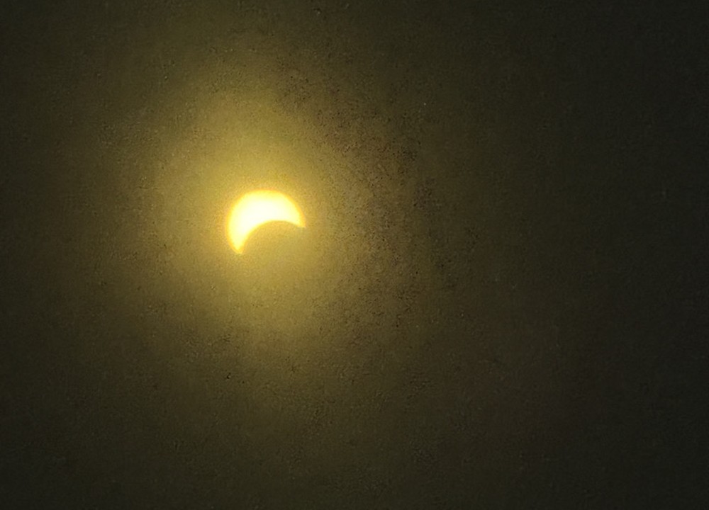 Photograph of a partial solar eclipse, the crescent Sun glowing through haze.